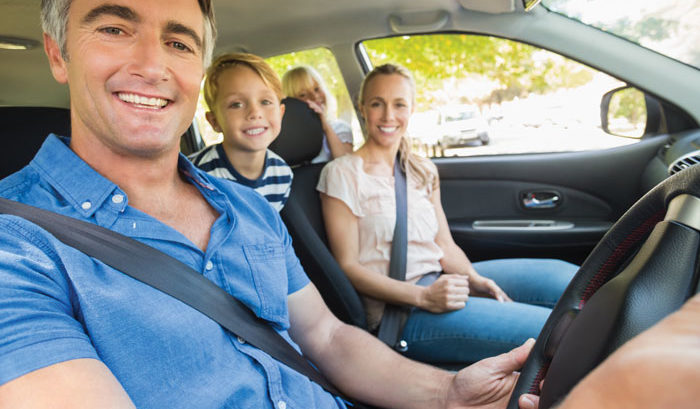 older man in blue collar shirt smiling in car with family