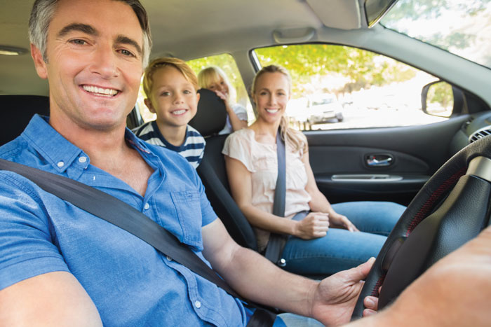 older man in blue collar shirt smiling in car with family