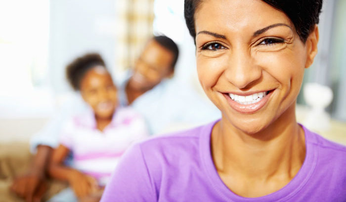 smiling ethnic woman with short hair and purple shirt with happy family blurred behind