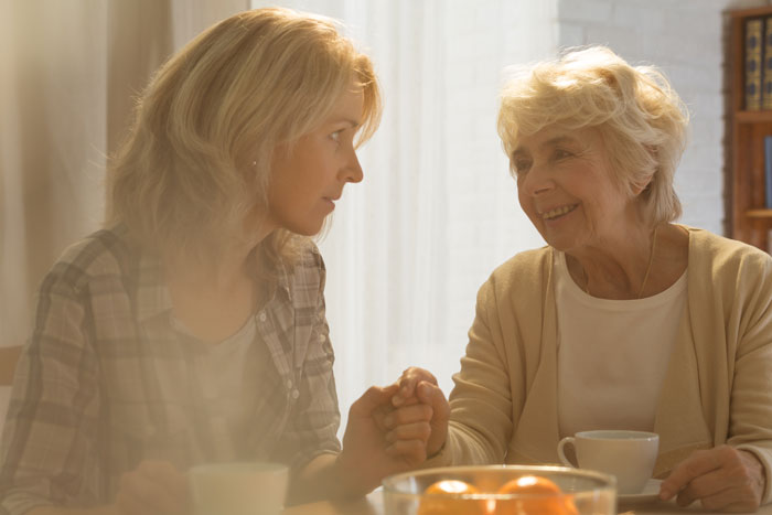 Middle-aged woman speaking with elderly mother at dining room table