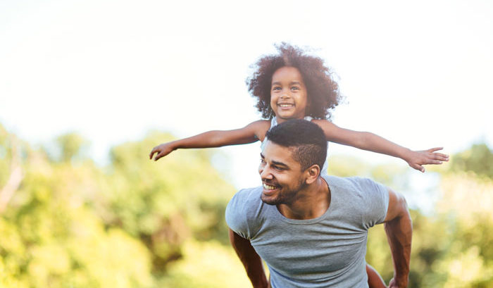 young biracial father with daughter on his back smiling with arms outspread