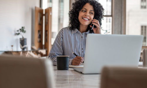 Smiling Woman Talking On Cellphone In Front Of Laptop