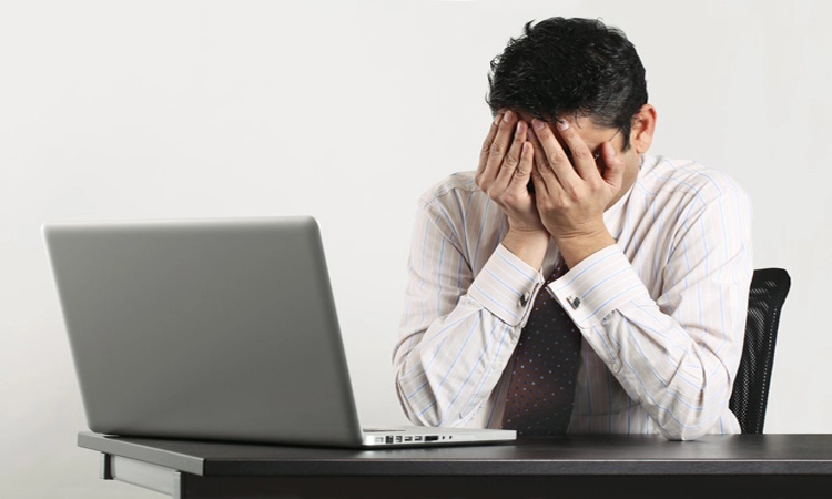Frustrated man in front of laptop computer with hands over face