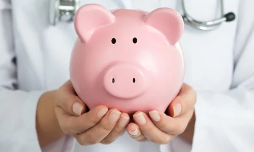 Close-up Of Healthcare Provider Holding A Piggy Bank